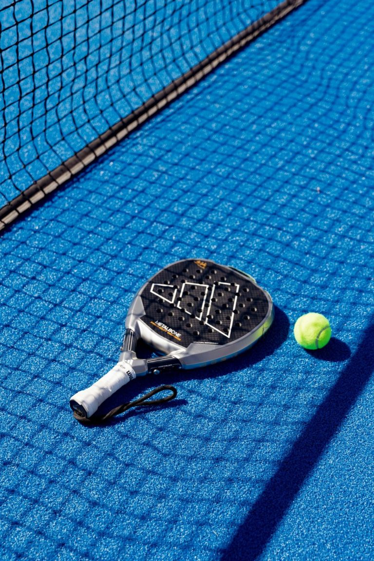 Raquette de padel et balle sur un court bleu.